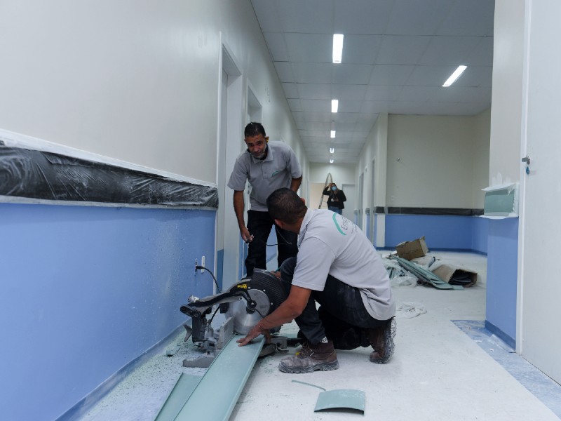 Foto da obra do Pronto-Socorro do HSPM. Dois homens trabalham nas obras do hospital. Um está conversando com o outro num corredor de paredes metade azul e metade branca